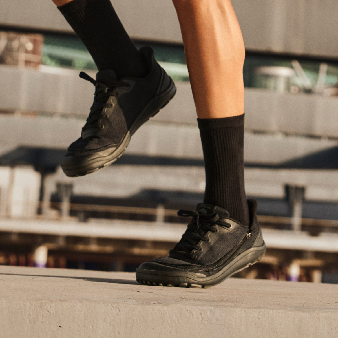 Person in black Arc trainers and black socks moving on an outdoor concrete platform.