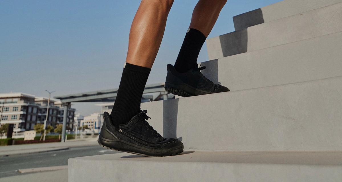Person stepping up concrete stairs in black Arc trainers and black socks.