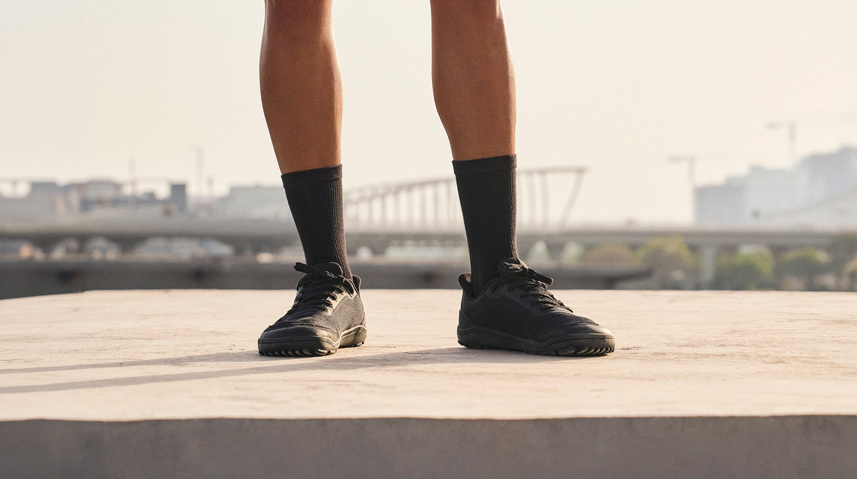 Person standing outdoors in black Arc trainers and black socks.