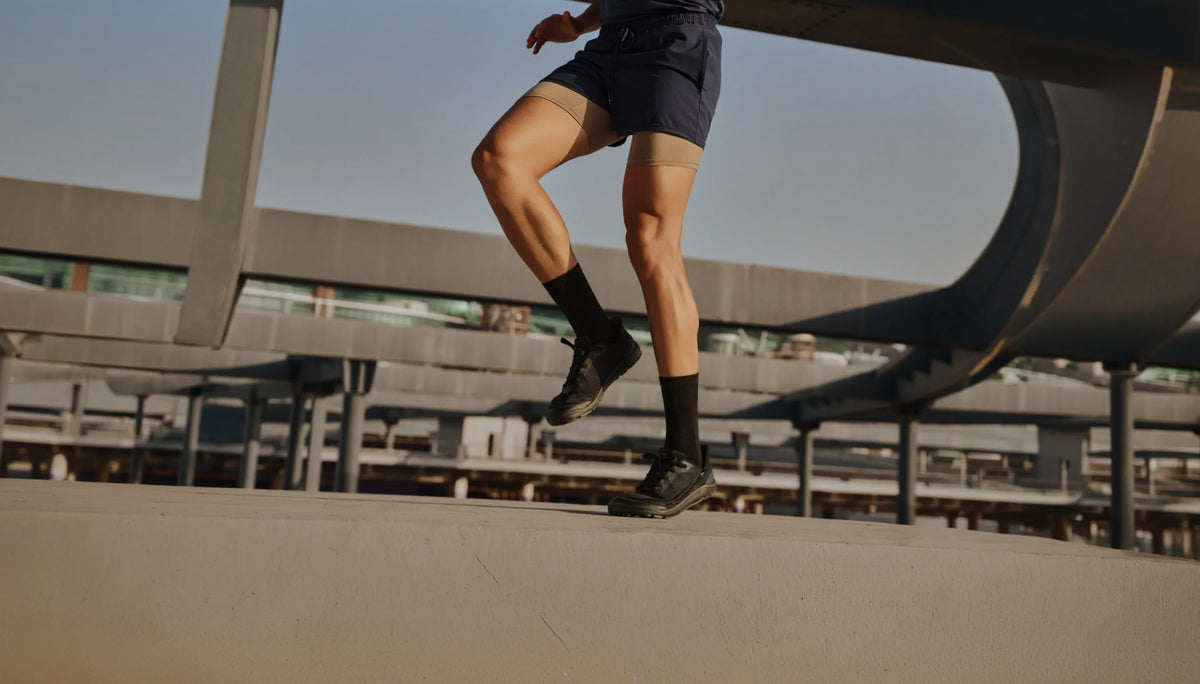 Person in black Arc trainers and black socks moving on an outdoor concrete platform.